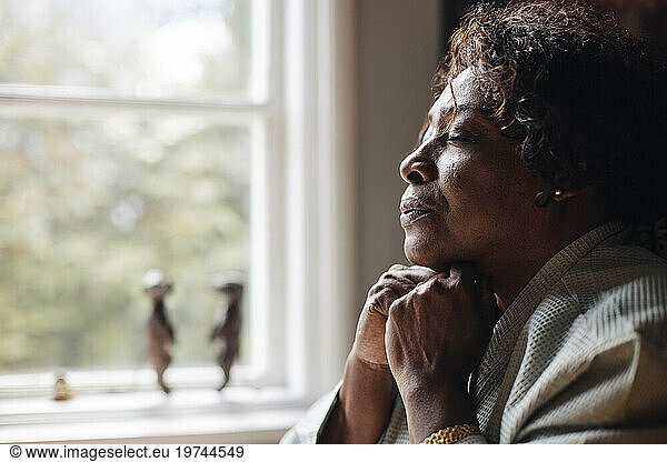 Mature woman with hand on chin and eyes closed doing breathing exercise at home