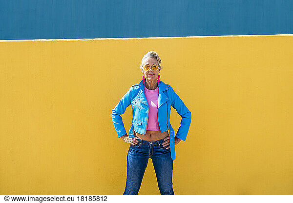 Mature woman with hand on hip in front of colored wall