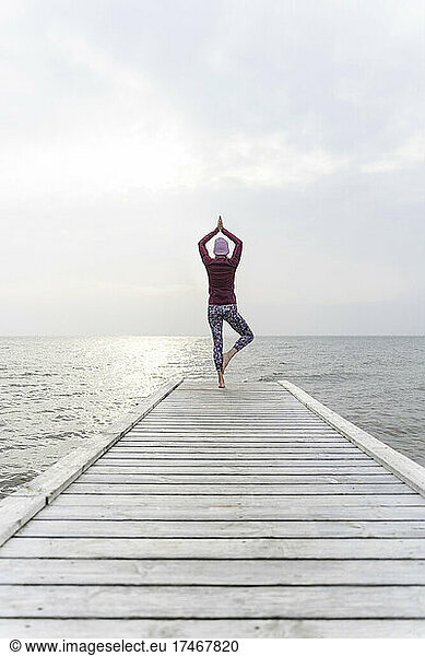 Mature woman with hands clasped practicing yoga on pier