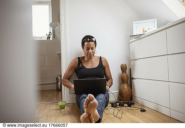 Mature woman working from home at laptop on floor