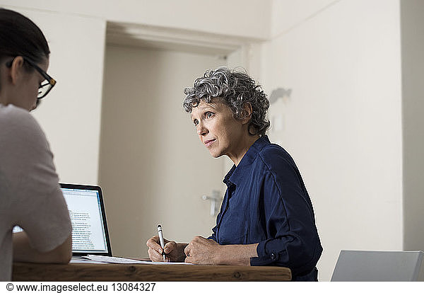Mature woman writing while working with colleague at home