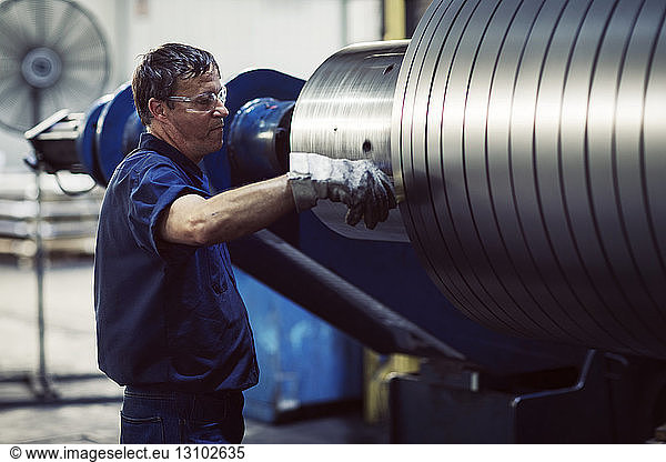 Mature worker examining in steel sheets rolling on machine at industry