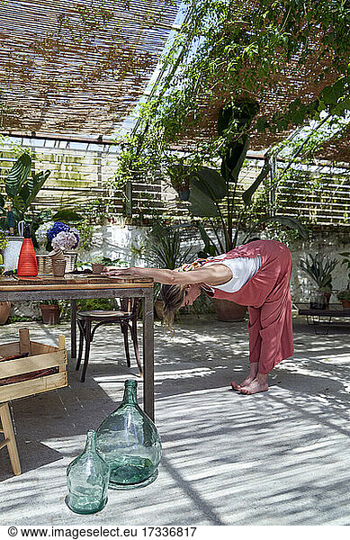 Maturing woman stretching while standing by table at backyard