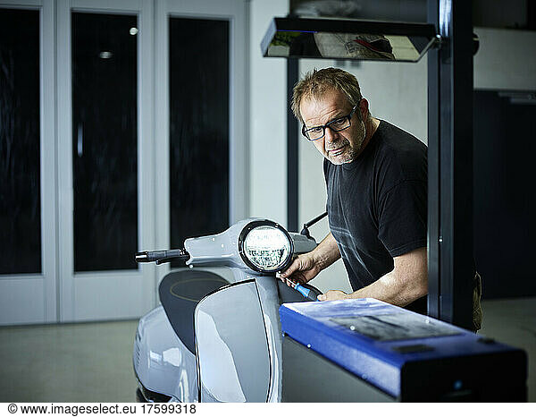 Mechanic adjusting headlight on motor scooter at auto repair shop