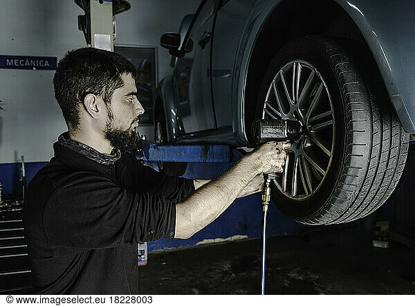 Mechanic with screwdriver repairing car wheel in workshop