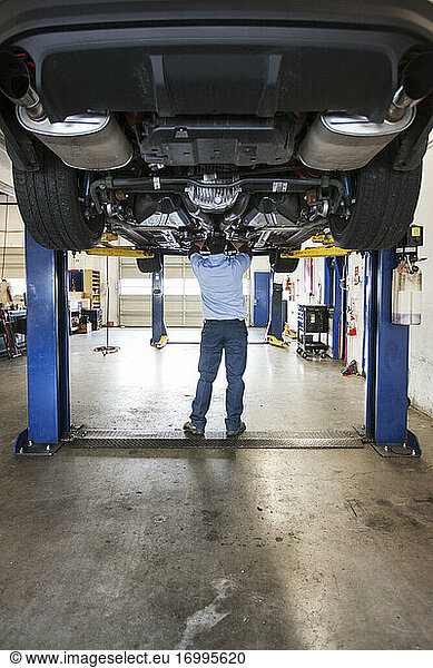 Mechaniker in einer Werkstatt arbeitet an der Unterseite eines Autos auf einer Hebebühne