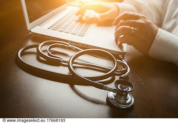Medical stethoscope resting on desk as male hands type on computer keyboard