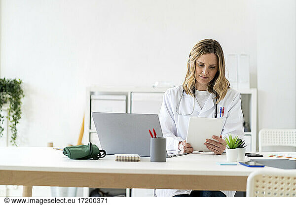 Medizinische Fachangestellte benutzt ein Tablet  während sie am Schreibtisch in einer medizinischen Klinik sitzt