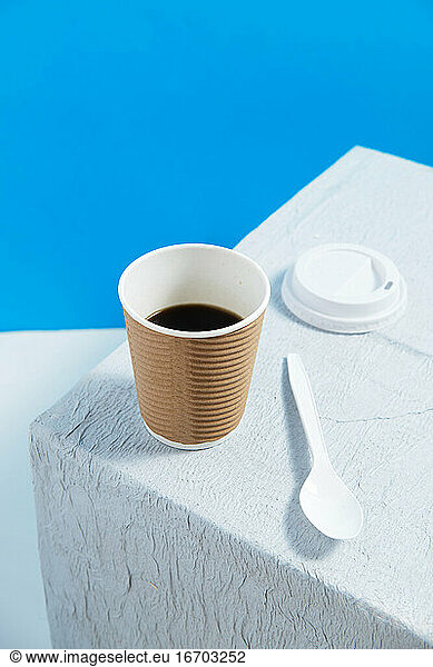 Mehrwegbecher mit Kaffee auf weißem Tisch mit weißem Plastikdeckel und Spo