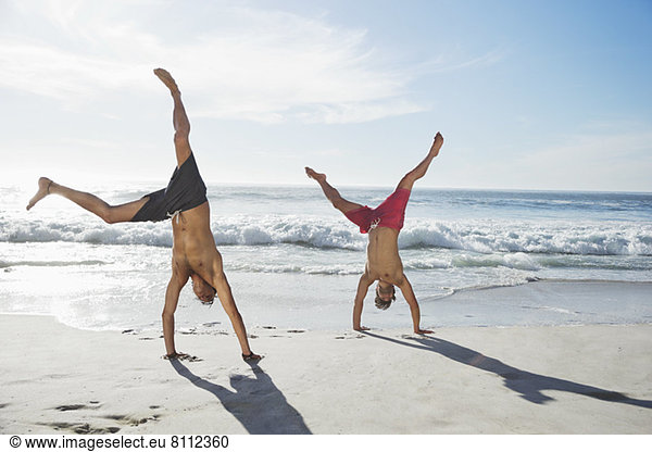 Men in swim trunks doing handstands on beach