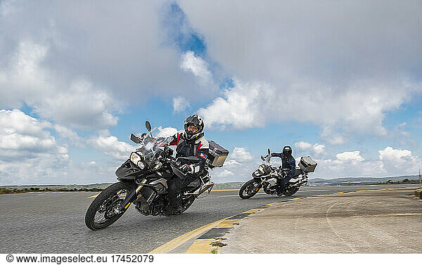 men leaning their adventure motorbikes into turn on road trip