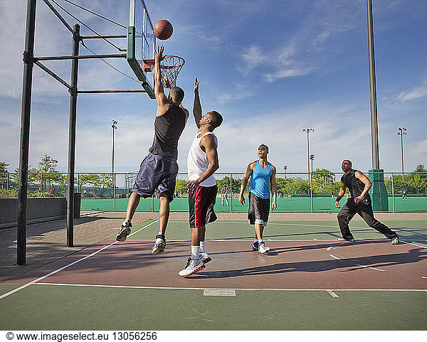 Men playing basketball in court on sunny day