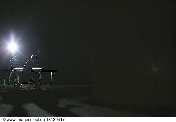 Men playing table tennis against light at night