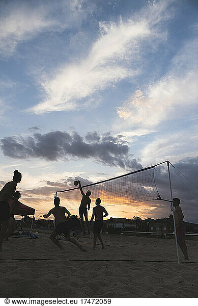 Men playing volleyball at beach at sunset