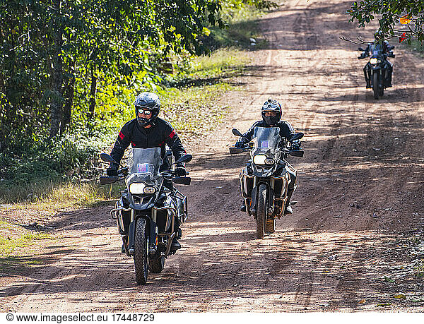 Men riding their adventure motorbikes on dusty road in Cambodia