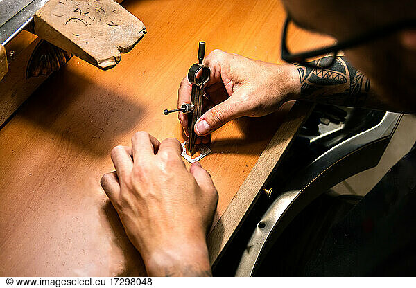 Men's hands in a jewelery workshop marking silver piece with compass