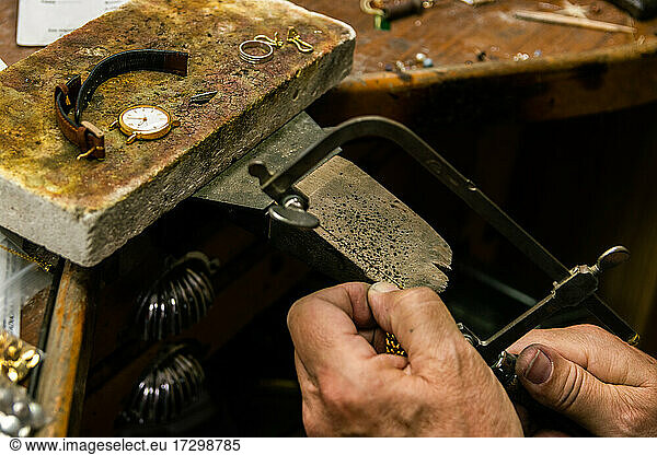 Men's hands in a jewelry workshop cutting piece of gold with hacksaw