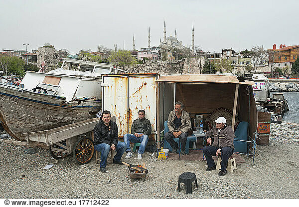 Men Sitting Outside A Shed On The Shore Beside A Boat On A Trailer; Istanbul  Turkey