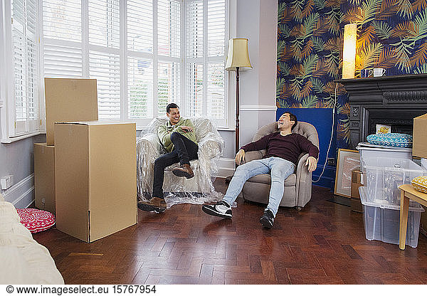 Men taking a break from moving house  relaxing and laughing in armchairs