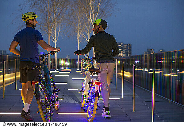 Men walking illuminated bicycles on urban footpath  London  UK