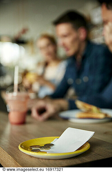 Menschen an einem Cafe-Tisch  eine Untertasse mit Kassenbon und Barzahlung