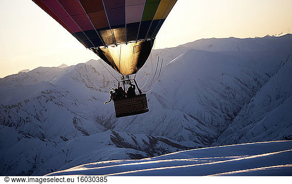 Menschen in einem Heißluftballon mitten in der Luft über einem schneebedeckten Berg.