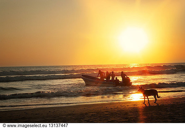 Menschen segeln Boot am Ufer bei Sonnenuntergang