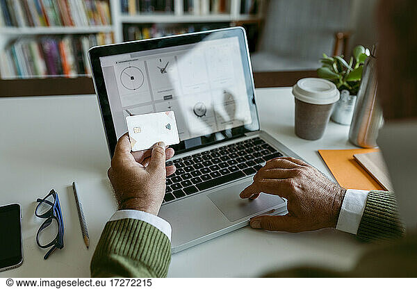 Menschliche Hand  die eine Kreditkarte benutzt  während sie zu Hause am Laptop arbeitet
