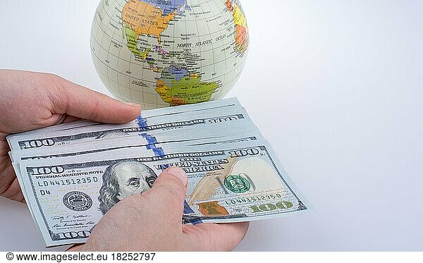 Menschliche Hand hält amerikanische Dollar-Banknoten an der Seite eines Modell-Globus auf weißem Hintergrund
