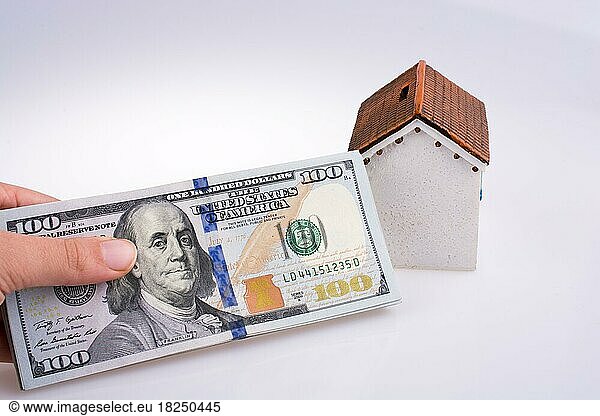Menschliche Hand hält amerikanische Dollar-Banknoten an der Seite eines Modellhauses auf weißem Hintergrund