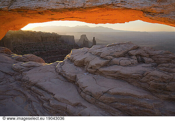 Mesa Arch of Canyonlands National Park in Utah glows orange as the morning sun bursts through this popular rock formation