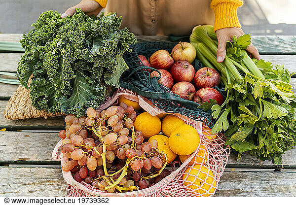 Mesh bags with fresh fruits and vegetables on table at farmer's market