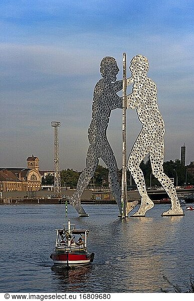Metallic sculpture called Molecule Man by Jonathan Borofsky in Spree River Berlin. Molecule Man is a series of aluminium sculptures  designed by American artist Jonathan Borofsky  installed at various locations in the world  including Berlin  Germany  and Council Bluffs  Iowa  USA.The first Molecule Man sculptures were made in 1977 and 1978 in Los Angeles  USA. The sculptures consist of three humans leaning towards each other  the bodies of which are filled with hundreds of holes  the holes representative of 'the molecules of all human beings coming together to create our existence'. A related sculpture is the Hammering Man.