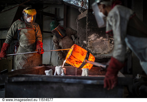 Metalworkers working in foundry  pouring molten bronze
