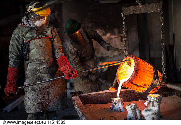 Metalworkers working in foundry  pouring molten bronze
