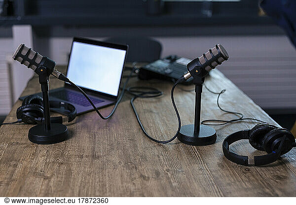 Microphones with headset and laptop on desk in recording studio