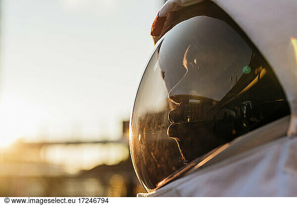 Mid adult astronaut wearing space helmet looking away during sunset