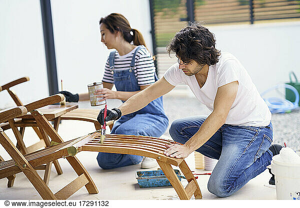 Mid adult boyfriend and girlfriend painting deck chair in new house