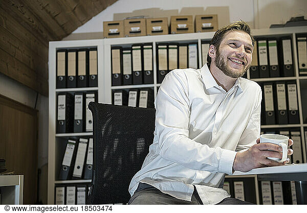 Mid adult businessman drinking coffee in an office and smiling  Bavaria  Germany