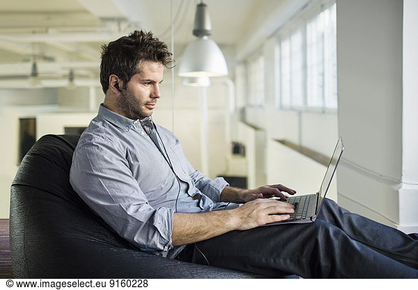 Mid adult businessman using laptop while sitting on bean bag in office