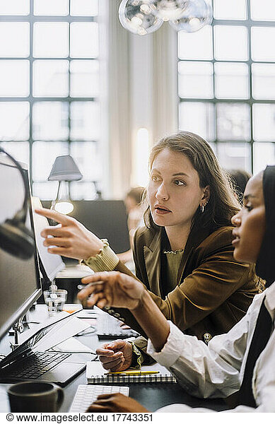 Mid adult businesswoman discussing over desktop PC with female colleague in office