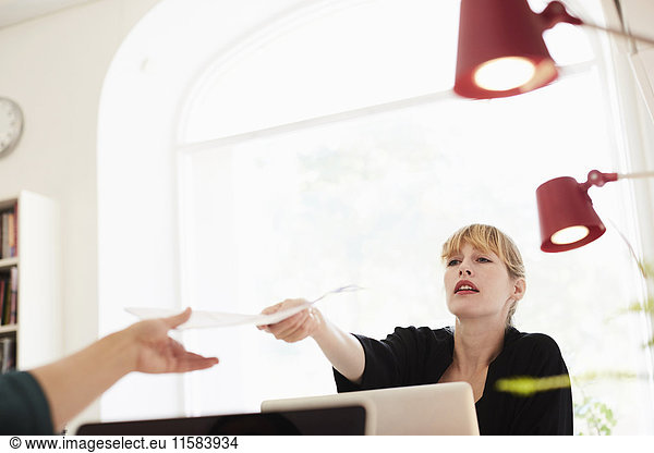 Mid adult businesswoman giving document to colleague in office