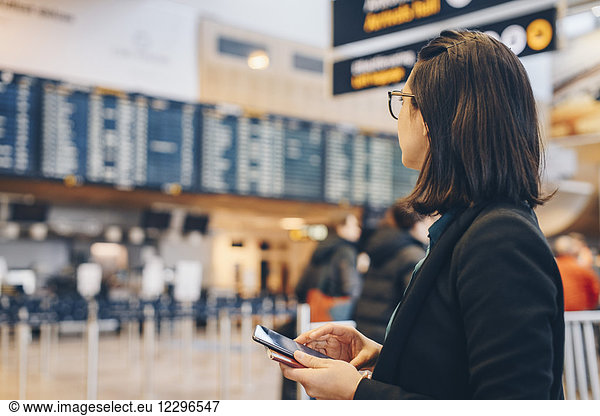 Mid adult businesswoman holding mobile phone while standing in airport