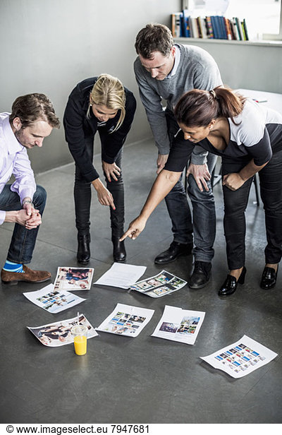 Mid adult businesswoman pointing at photographs while discussing with colleagues in office
