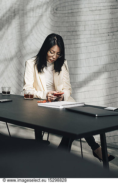 Mid adult businesswoman using mobile phone at table in office