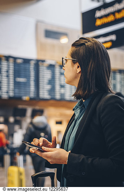 Mid adult businesswoman using mobile phone while standing in airport