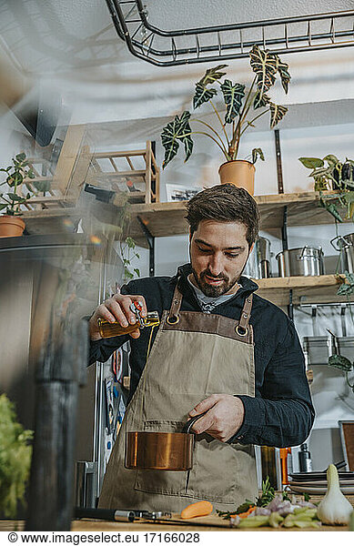 Mid adult chef pouring oil in cooking pan while working in kitchen