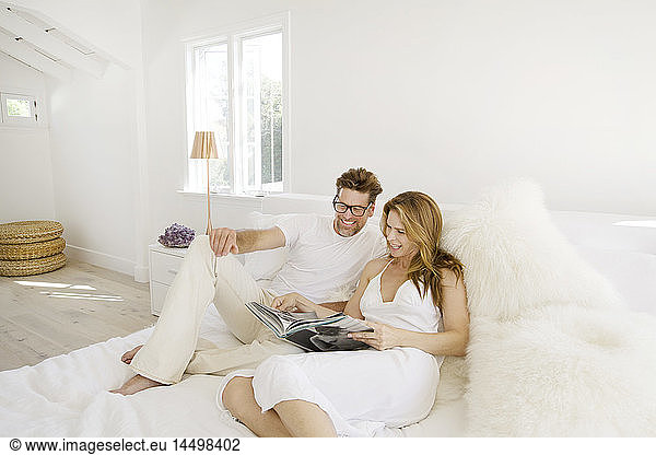 Mid-Adult Couple Looking at Book while Relaxing on Bed