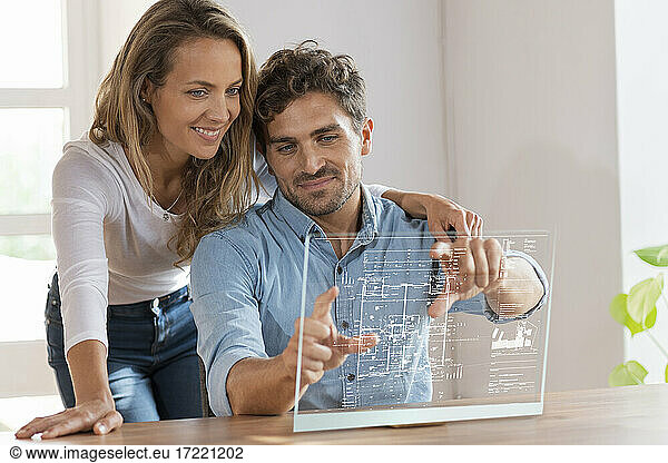 Mid adult couple looking at floor plan over transparent screen at home
