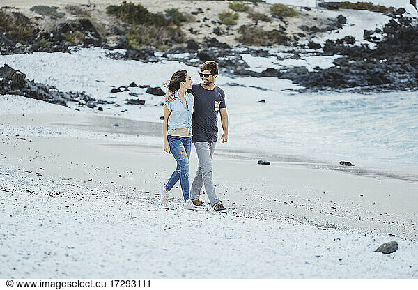 Mid adult couple talking while walking at beach